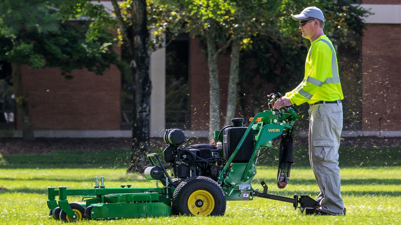 Man controls a walk-behind mower while standing on a sulky