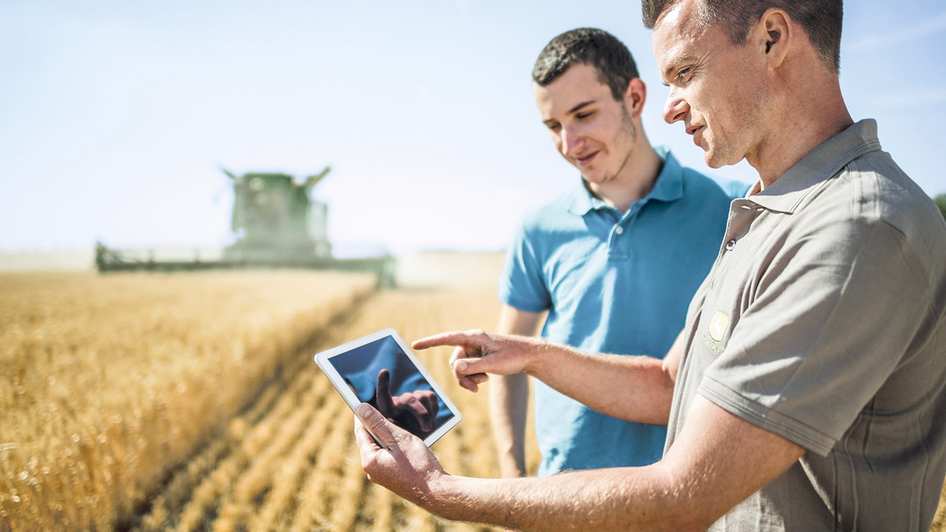 Image of 2 men looking at a tablet in a field being harvested