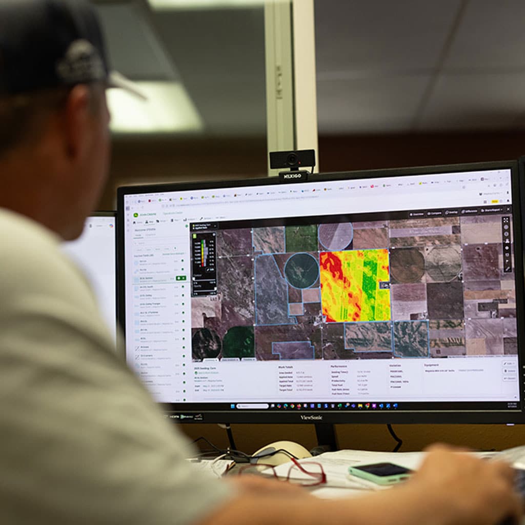 Person viewing a computer monitor displaying a color‑coded agricultural field map and analysis software.