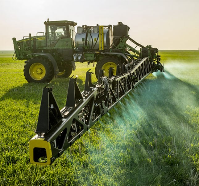 Self‑propelled agricultural sprayer applying liquid across a green field.