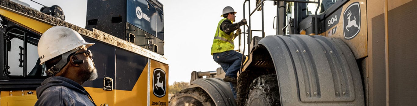 le conducteur d’une chargeuse à quatre roues motrices observe le technicien d’un concessionnaire grimper dans la machine