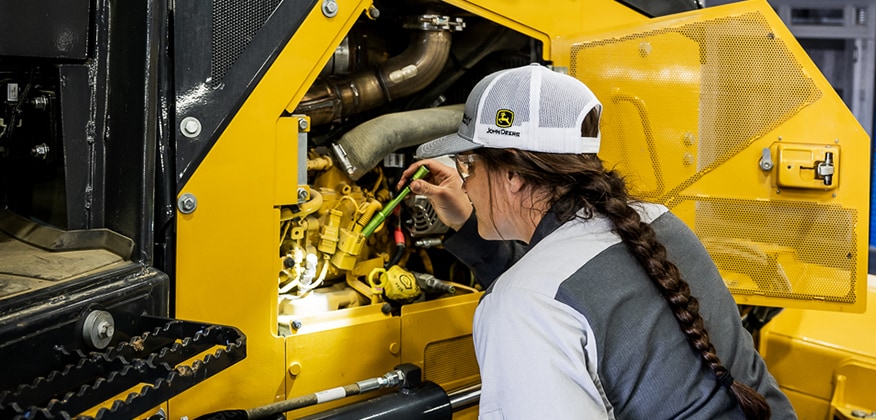 A female technician uses a flashlight to inspect an engine compartment.