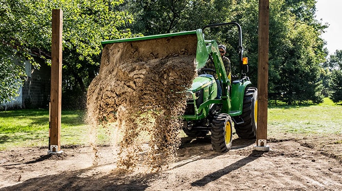 Tractor with loader dumping sand between two posts