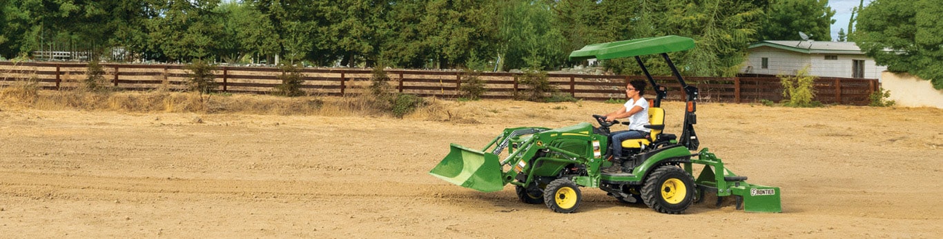 Person driving a John&nbsp;Deere 1 Series Sub-Compact Tractor through a dirt field.