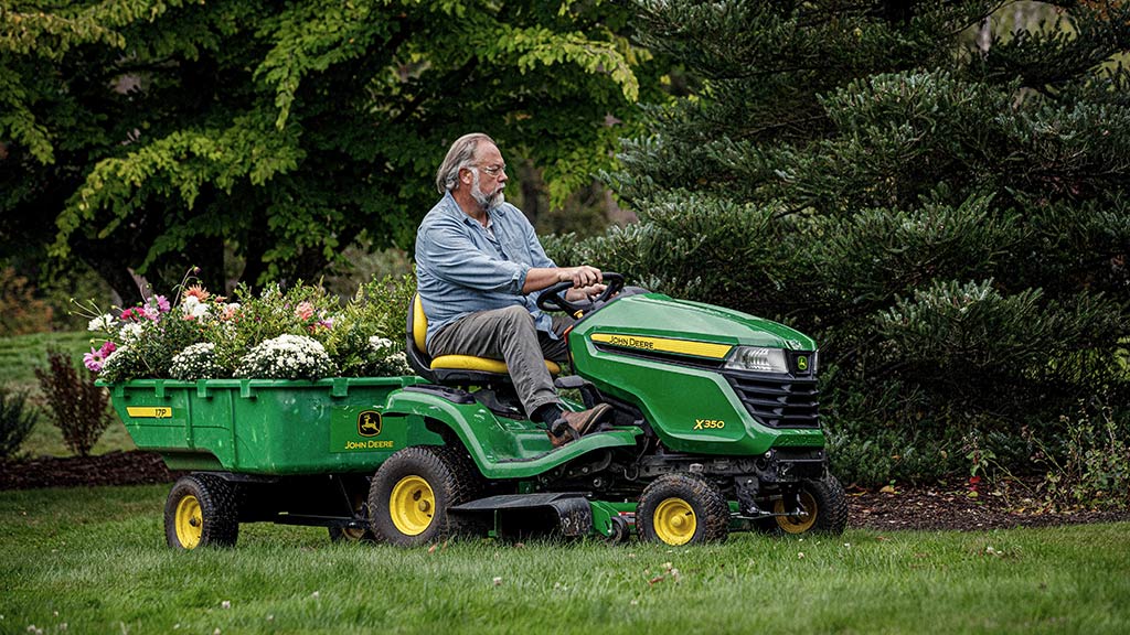 Personne tirant un massif de fleurs dans une remorque 17P avec un tracteur de pelouse X350.