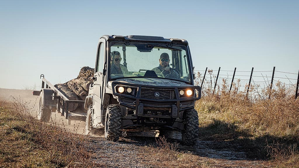 Couple pulling a trailer of logs in a XUV835M Gator(TM) XUV.