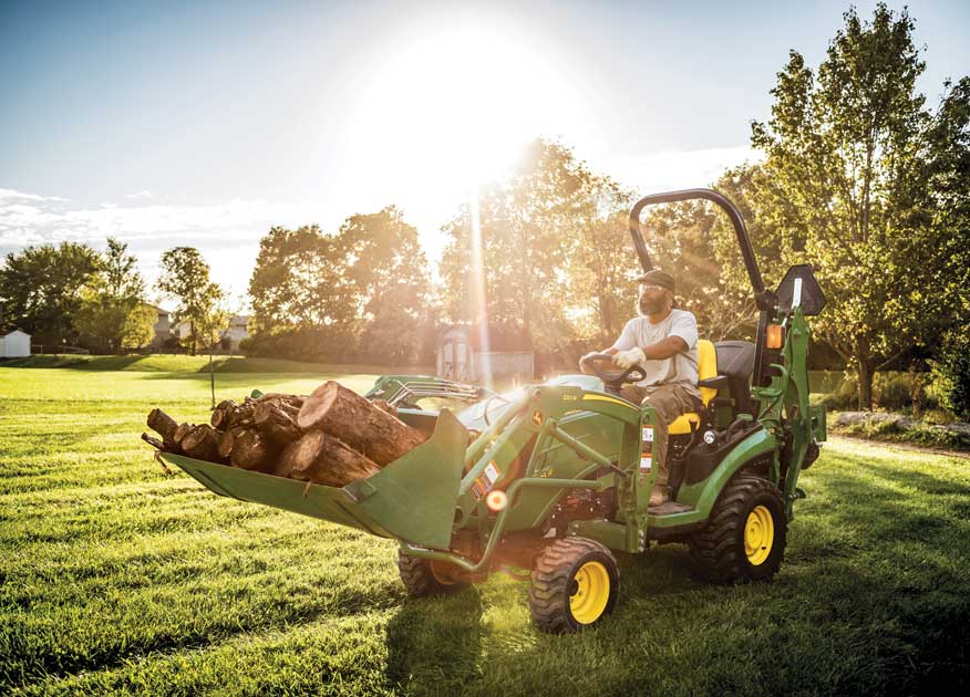 Homme conduisant un tracteur compact 1025R de John Deere équipé d'un godet 120R contenant des bûches