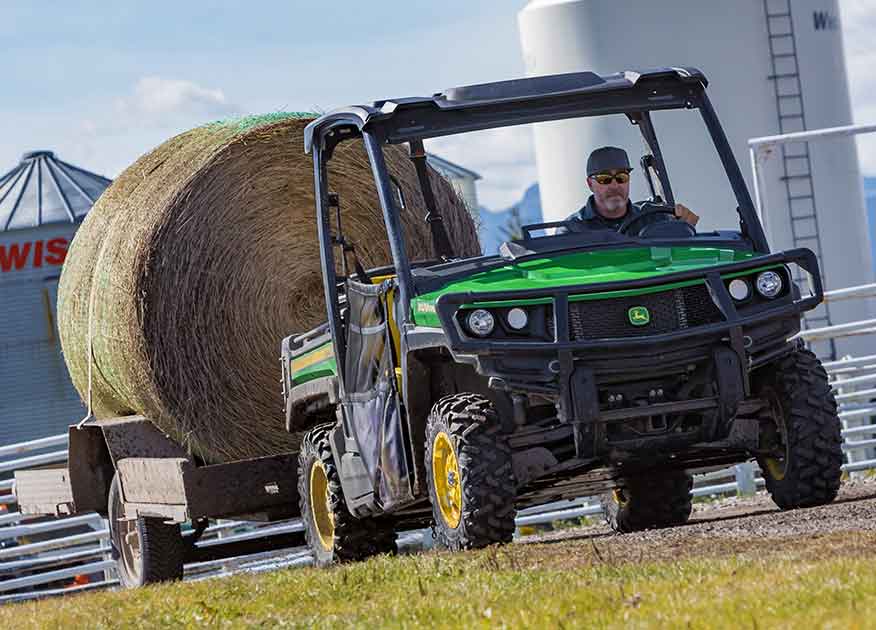 Man driving a John Deere Gator Utility Vehicle while towing a bale of hay