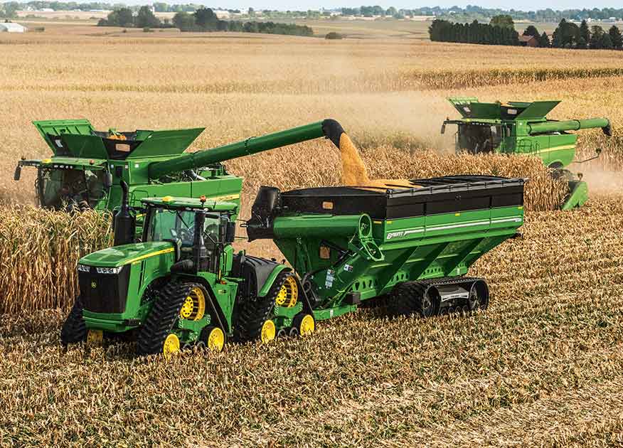 John Deere tractor and two combines working in a field