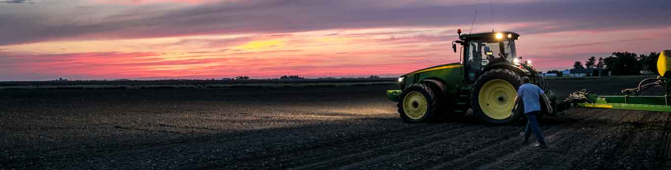 Homme marchant dans un champ à côté d'un tracteur John Deere au coucher du soleil