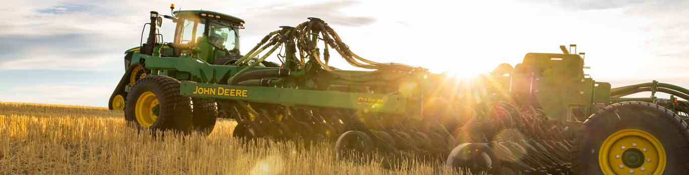 Tracteur de John Deere équipé d'un accessoire dans un champ au lever du soleil