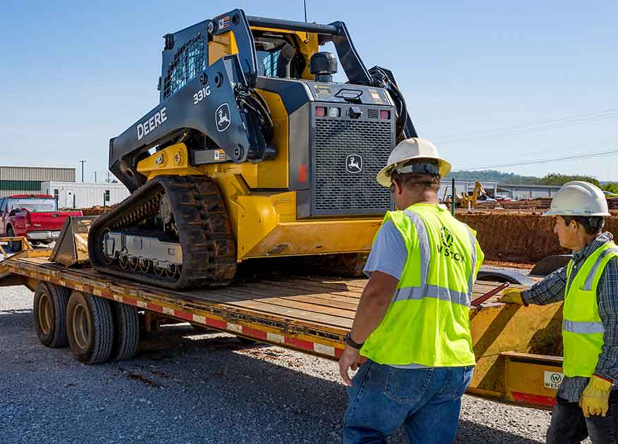 Deux hommes à côté d'une remorque transportant une chargeuse 331G de John Deere