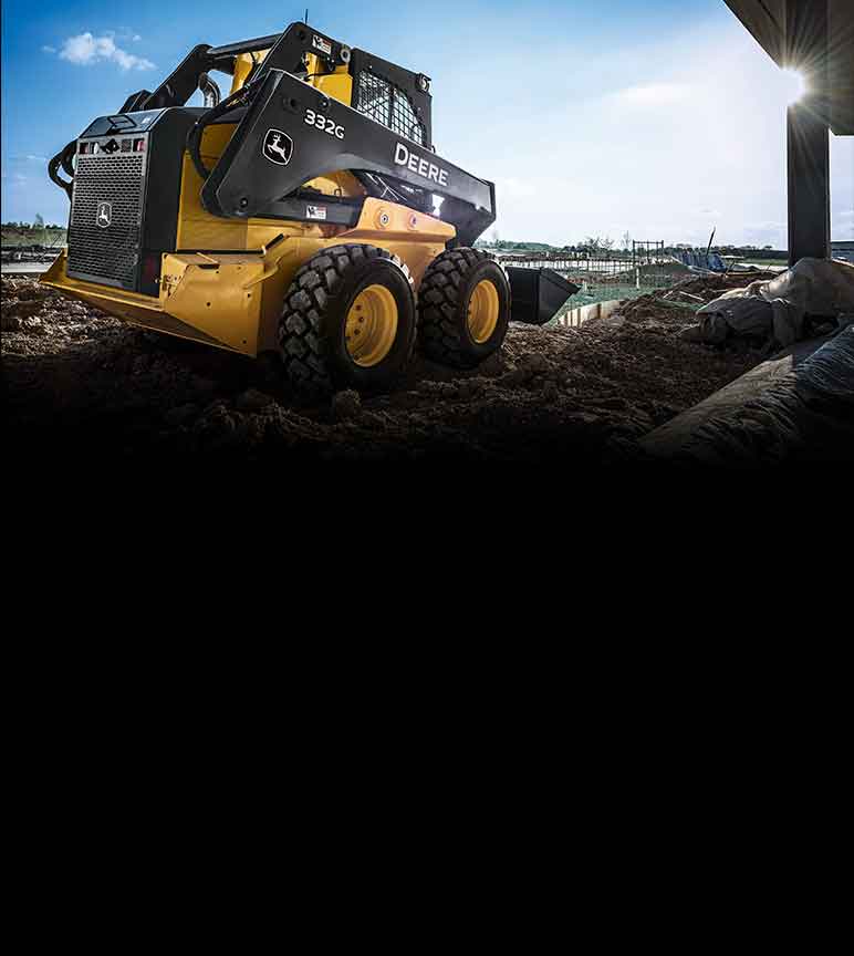 Vue de côté d'une chargeuse compacte 332G John Deere dans un champ de terre