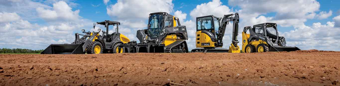 Équipement de construction compact de John Deere en rang dans un champ de terre