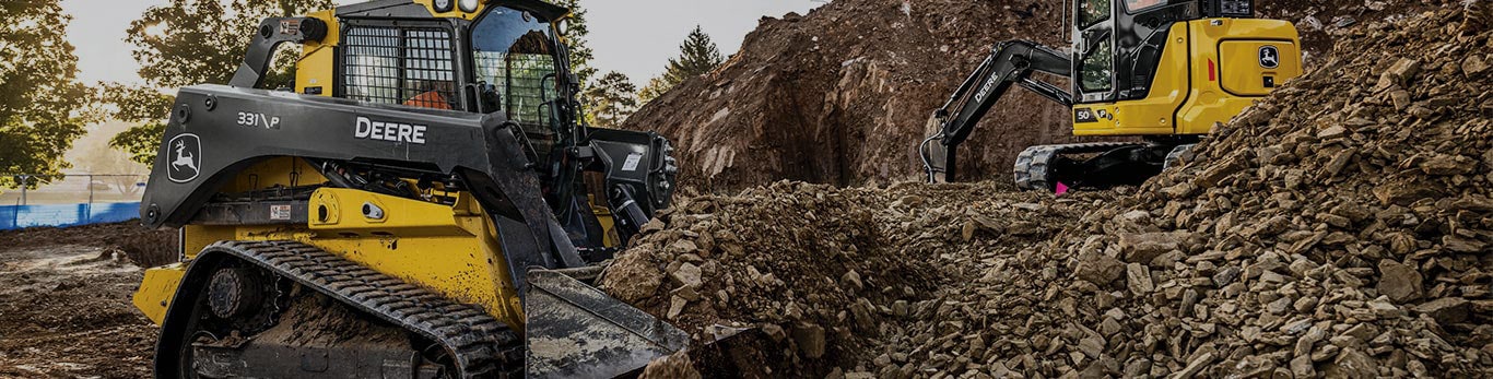 Chargeuse à chenilles compacte et mini-excavatrice John Deere déplaçant de la roche et du sol sur un chantier de construction.