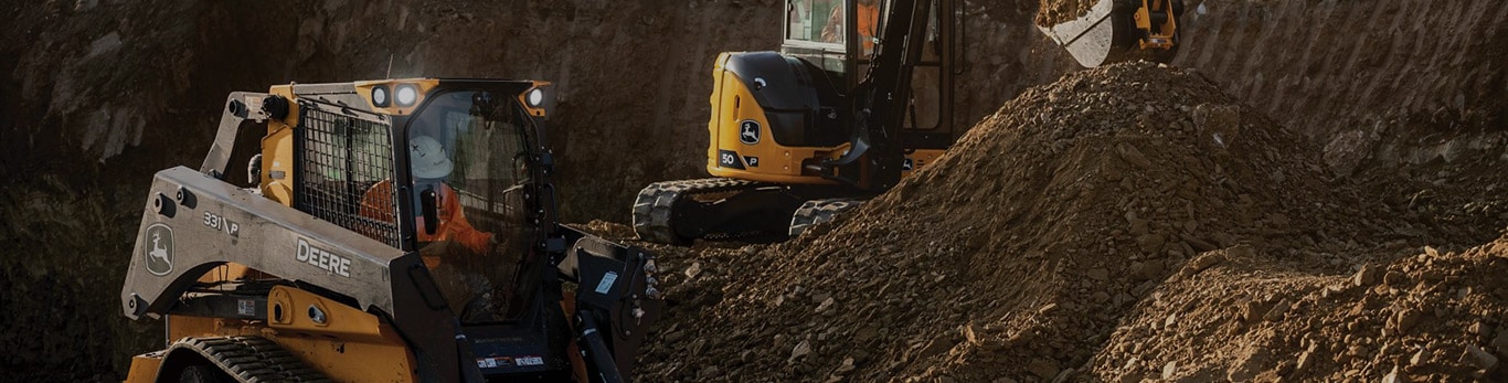 Chargeuse à chenilles compacte et mini-excavatrice John Deere déplaçant de la terre sur un site d’excavation.