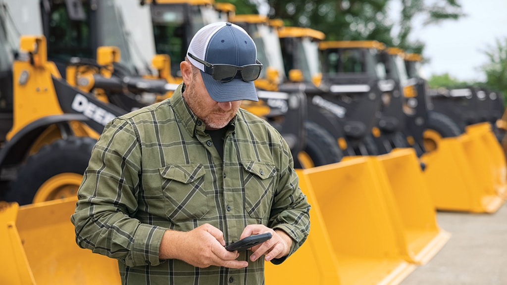 Personne utilisant un appareil mobile devant une chargeuse à roues John Deere stationnée.