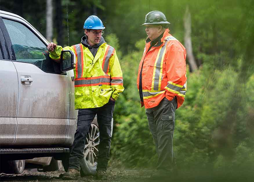 Two men wearing reflective vest and hard hats standing next to a truck