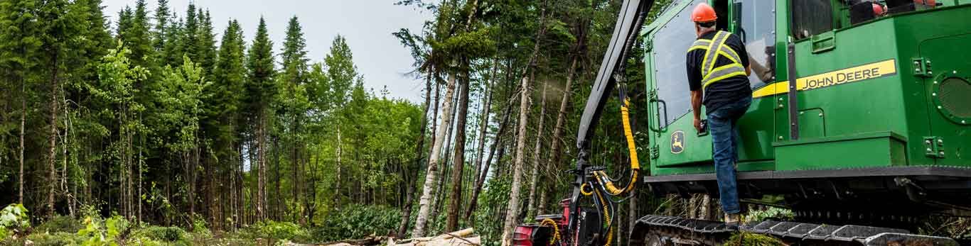 Homme debout sur de l'équipement de foresterie de John Deere dans un chantier d'exploitation forestière