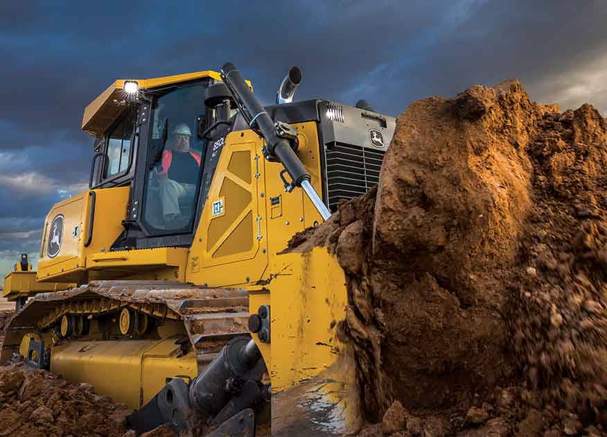 Homme utilisant un bouteur chenillé 850L de John Deere dans un champ de terre