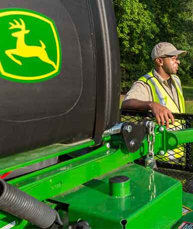 Two men talking next to John Deere landscaping equipment on a trailer