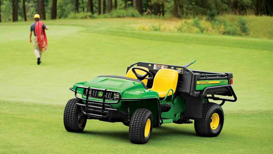 John Deere Gator utility vehicle on a golf course with a man walking in the background