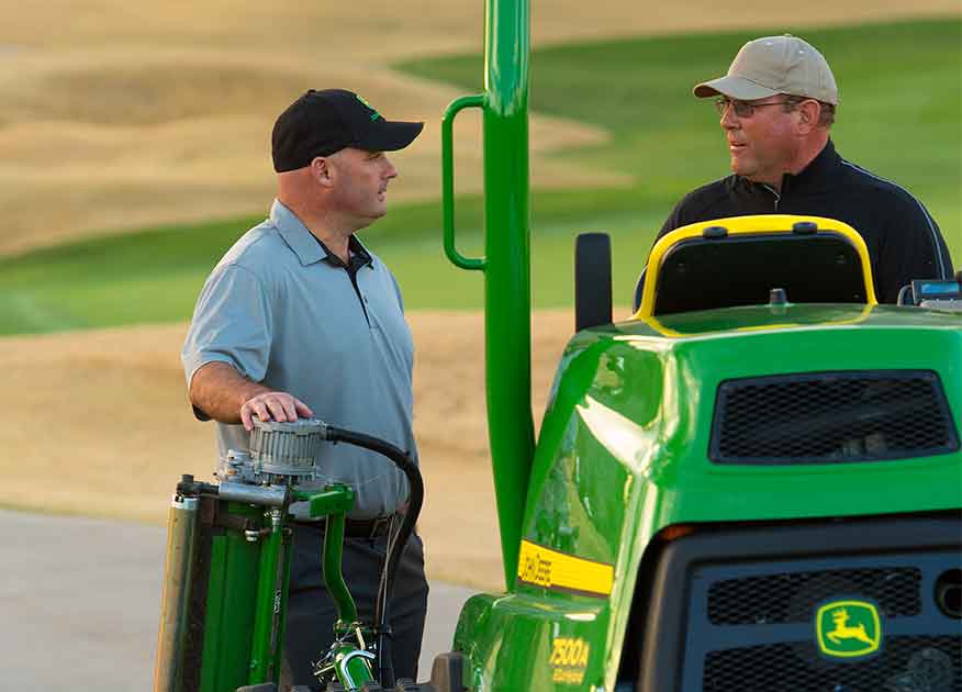 Two men on a golf course next to John Deere Sports Turf equipment