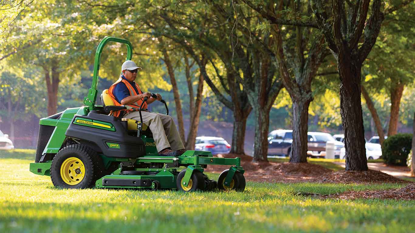 Homme portant une veste jaune et une casquette blanche exécutant des travaux d'aménagement paysager avec une tondeuse à rayon de braquage nul de John Deere