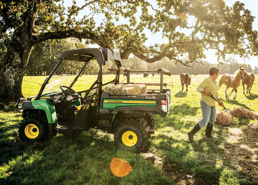 Woman loading hay into the bed of a John Deere Gator Utility Vehicle with horses in the background