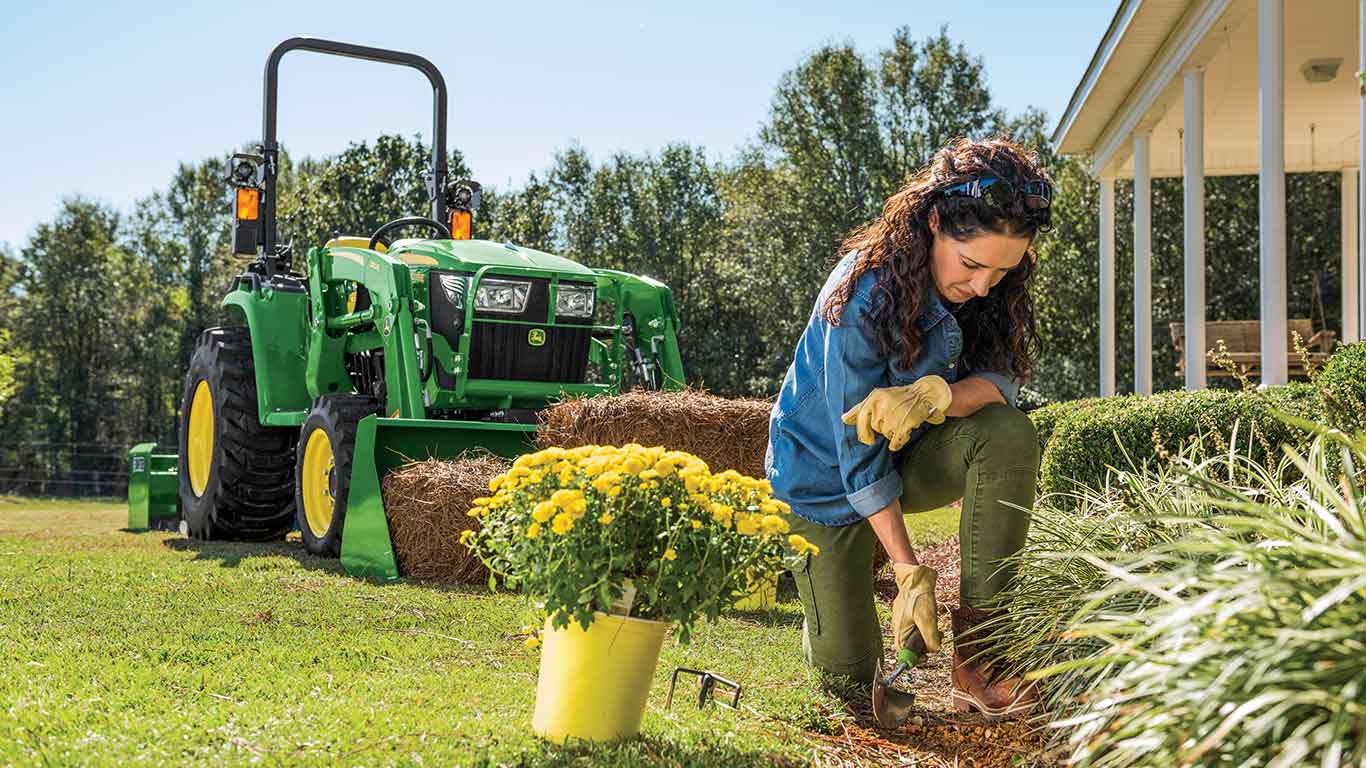 Image d'une femme qui jardine avec en arrière-plan un tracteur compact de John Deere doté d'un godet.