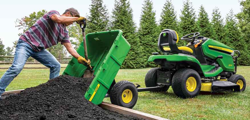 Man scooping soil out of a 10P poly cart that is attached to a John Deere Lawn Tractor