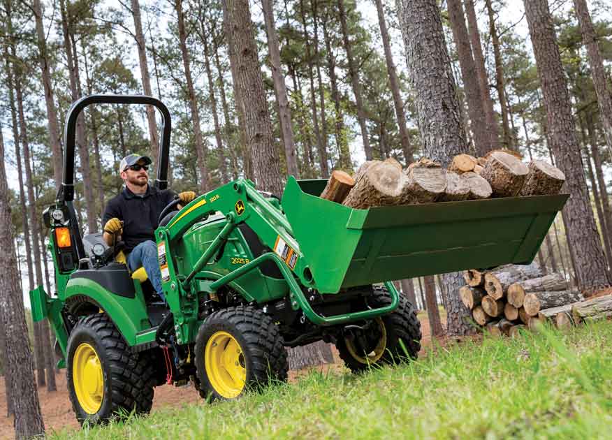 Homme qui utilise un tracteur compact 2025R de John Deere doté d'un godet pour transporter des grumes