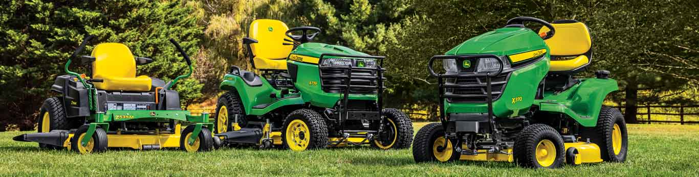 Des tracteurs de pelouse John Deere et une tondeuse à rayon à braquage nul ZTrak de John Deere garés devant des arbres.