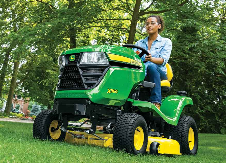 Woman operating a John Deere X380 Select Series Lawn Tractor in a yard