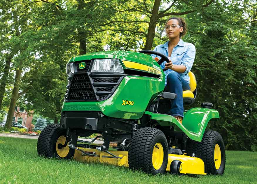 Une femme aux commandes d'un tracteur Select Series X380 de John Deere dans un jardin