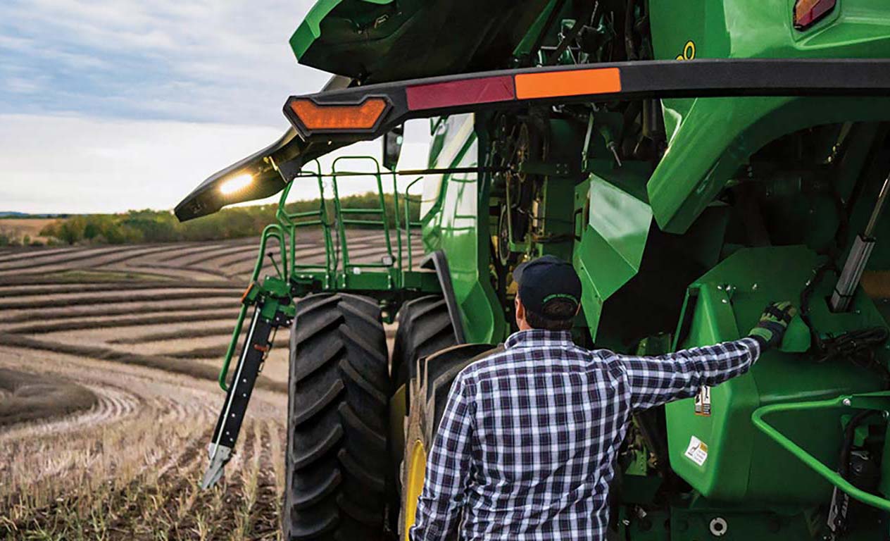 A person standing next to a Combine in a field with harvested rows