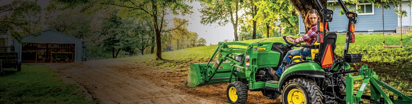 Femme conduisant un tracteur compact 1025R avec chargeur et boîte à lames pour mettre à niveau son allée