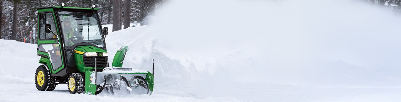 A woman clearing snow from a path with a John Deere X758 lawn tractor and snowblower attachment.