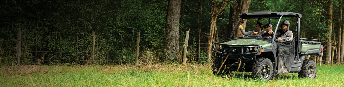 Men driving an open-station John Deere Gator&trade; XUV 845M through a wooded property