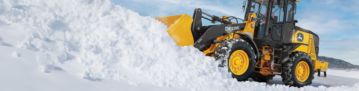 Chargeuse à roues 444G équipée d'une lame de déneigement qui déblaie la neige devant un ciel bleu. 