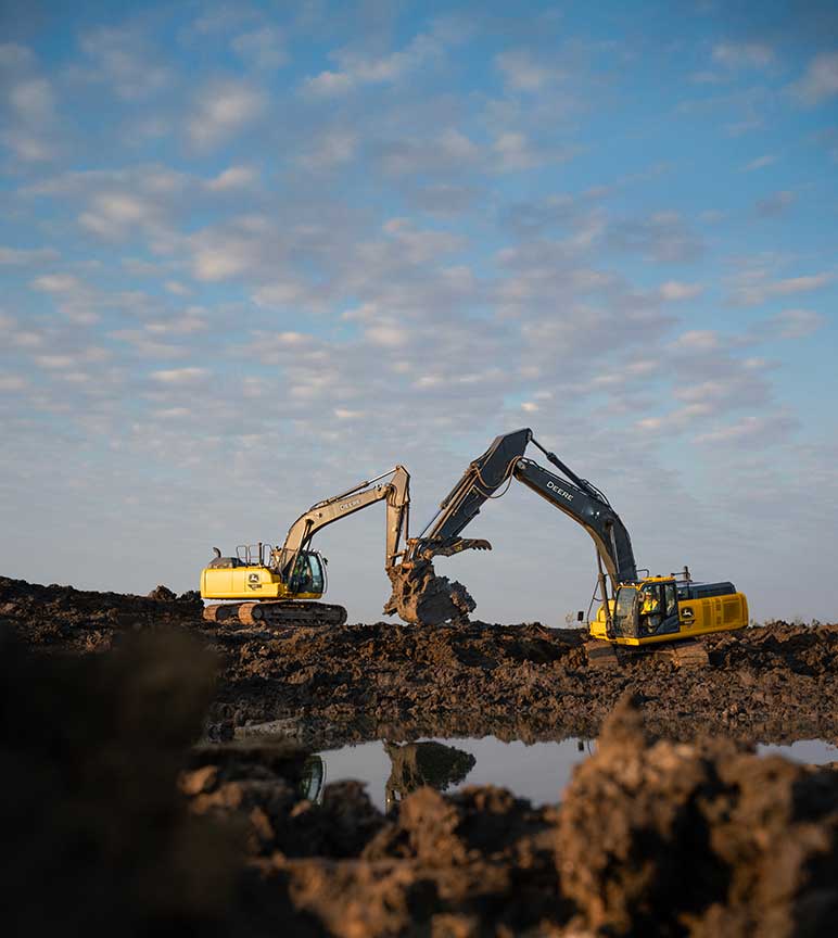 Deux grandes excavatrices jaunes de John Deere creusant une tranchée dans un terrain en friche