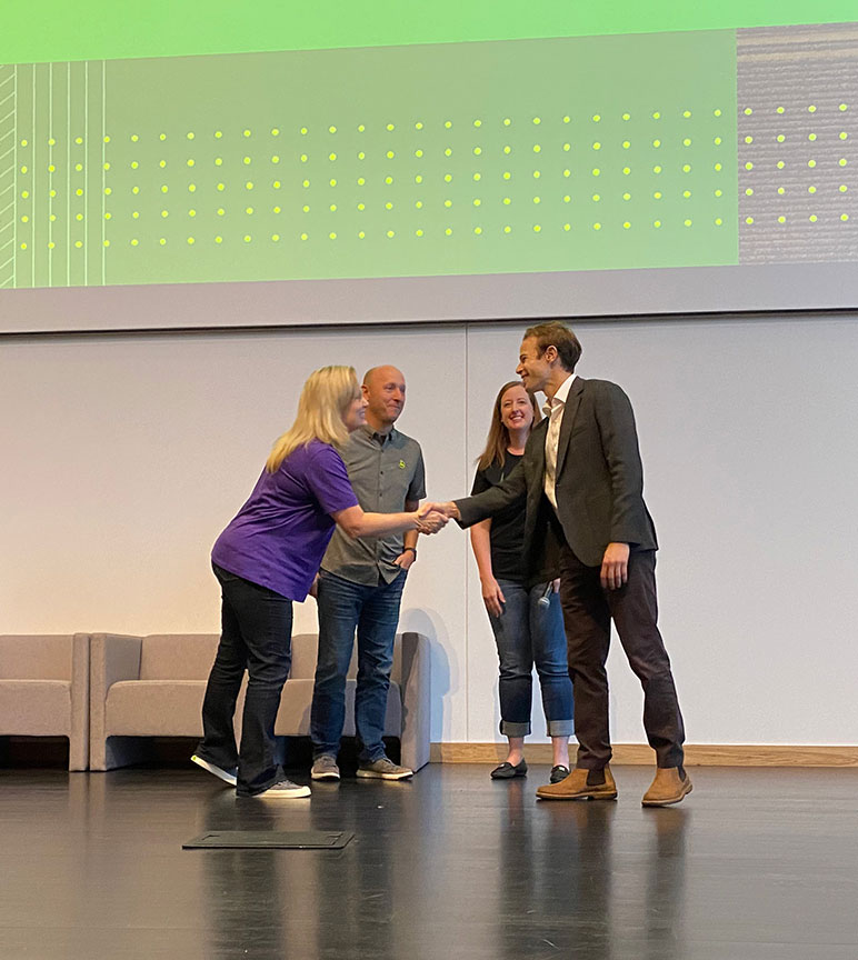 Deere employees shake hands on a stage with the CEO of Albedo.