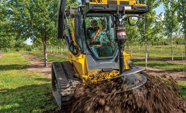 Chargeuse à direction différentielle de John Deere équipée d'une tarière à transmission à engrenage planétaire en train de creuser un tunnel dans la terre et d'en rejeter l'excès