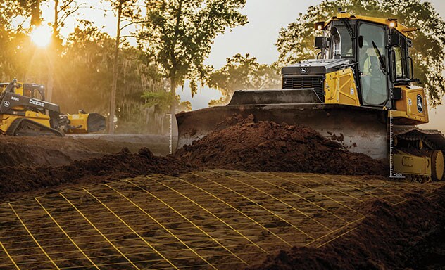 Le camion articulé à benne basculante de John Deere nivelant le terrain sur le chantier tandis que la chargeuse à direction différentielle 333G fonctionne à l’arrière. Une superposition de grille jaune illustre le logiciel de construction de précision.
