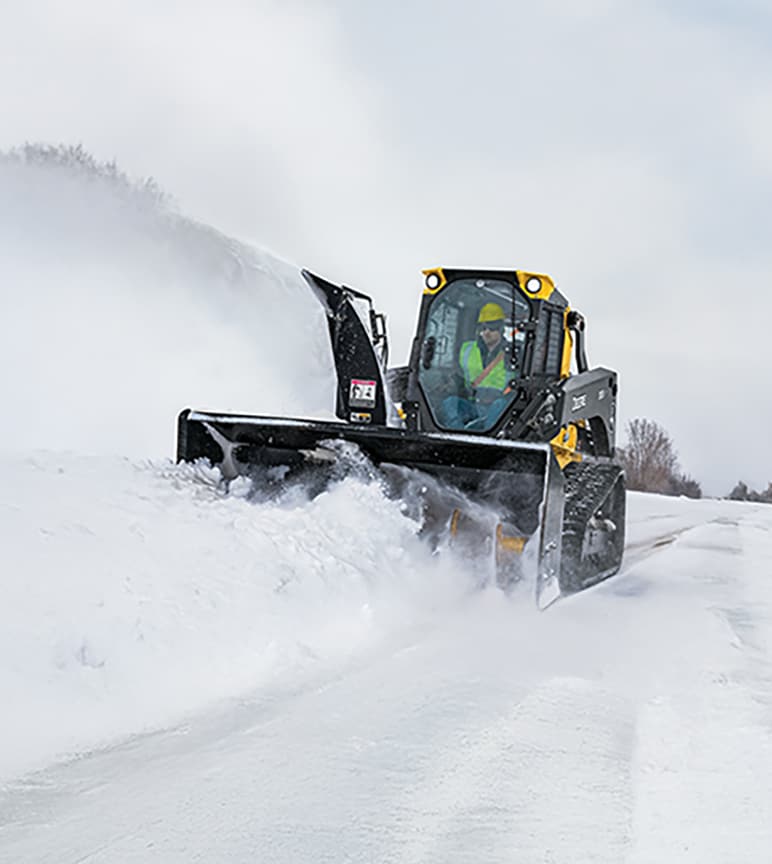 Crawl Track Loader with snow blower attachment driving on a snowy path.