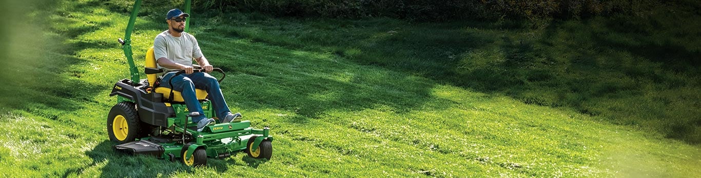 A man driving a John Deere 1025R Compact Tractor with loader attachment from snow-covered grass to blooming fields.