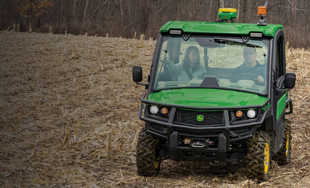 Two people driving XUV835R Gator Utility Vehicle in a harvested corn field