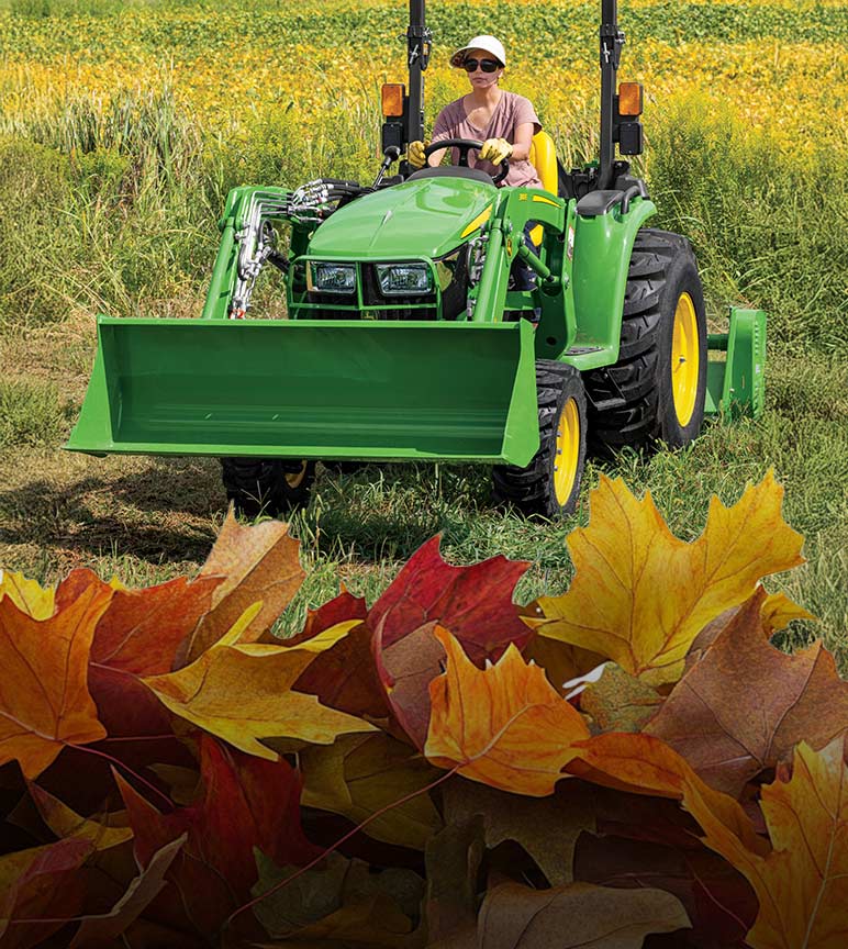 Woman driving a 4044M Compact Tractor with its front scoop up and fall leaves in the foreground.