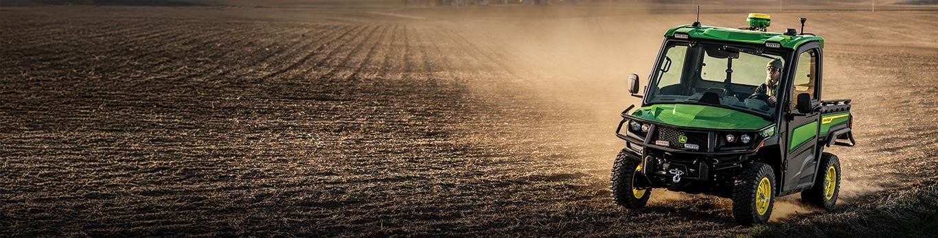 A woman driving a John Deere Gator™ XUV Utility Vehicle through a dusty farm field.
