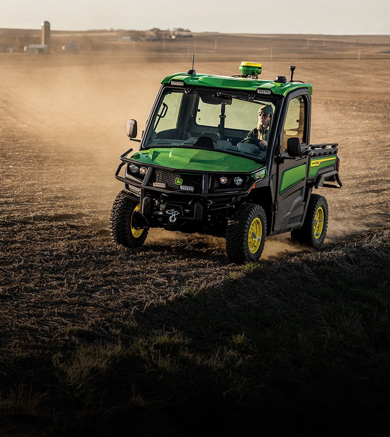 A woman driving a John Deere Gator™ XUV Utility Vehicle through a dusty farm field.